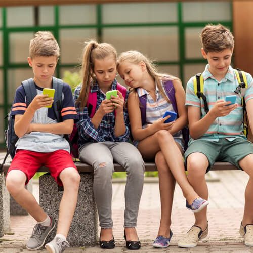 Group of four children seated and looking at their phones.
